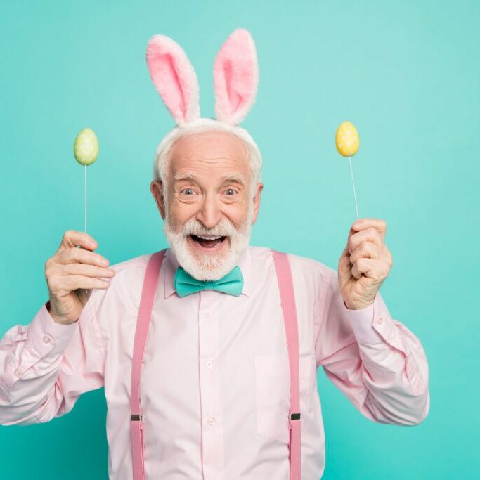 Portrait of astonished funky crazy excited old man hold stick with colorful eggs, enjoy easter party event wear pink hare headband pink shirt isolated over turquoise color background